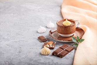 Cup of hot chocolate and pieces of milk chocolate with almonds on a gray concrete background with