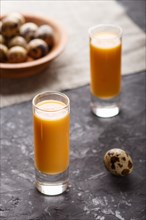 Sweet egg liqueur in glass with quail eggs on a black concrete background. Side view, low key,