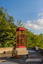 Red wooden telephone booth minus phone and without glass on roof of building on sunny day with blue