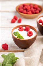 Yogurt with raspberry in clay cups on white wooden background and linen textile. Side view, close