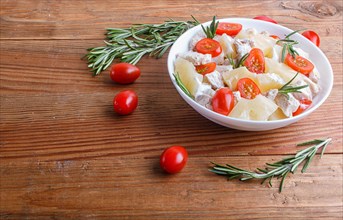 Chicken fillet salad with rosemary, pineapple and cherry tomatoes on brown wooden background. close