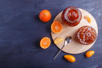 Tangerine and kumquat jam in a glass jar with fresh fruits on a black wooden table. Homemade, copy