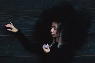 Female white blonde model wear black furry hat leaning by her side against a wooden wall, holding
