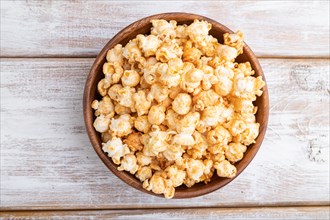 Popcorn with caramel in wooden bowl on a white wooden background. Top view, flat lay, close up