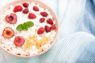 Rice flakes porridge with milk and strawberry in ceramic bowl on white concrete background and blue