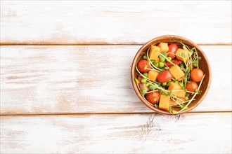 Vegetarian vegetable salad of tomatoes, pumpkin, microgreen pea sprouts on white wooden background.