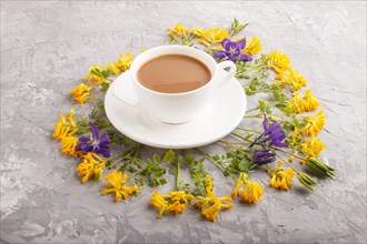 Yellow and blue flowers in a spiral and a cup of coffee on a gray concrete background. Morninig,