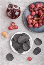 Black potato chips with charcoal, balsamic vinegar in glass, red grapes on a blue ceramic plate on