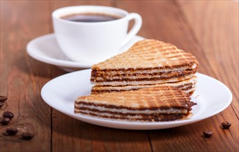 Waffle sandwiches with boiled condensed milk in plate on brown wooden table with cup of coffee.