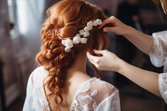 Close up of hairstylist arranging beautiful elegant red haired bridal hairstyle with flowers. KI