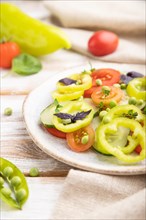 Vegetarian salad from green pea, tomatoes, pepper and basil on white wooden background and linen