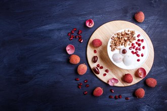 Greek yogurt with lychee, pomegranate seeds and granola in a white plate on a black wooden