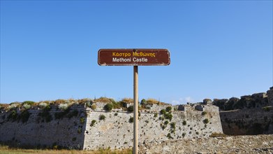 Brown signpost against a blue sky points towards Methoni Castle, Methoni sea fortress, Peloponnese,