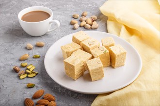 Traditional indian candy soan papdi in white plate with almond, pistache and a cup of coffee on a