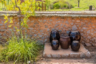 Ceramic fermentation jars sitting in front of mud and stone wall in urban public park in South