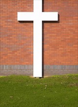 Large white crucifix cross against brick wall on grass lawn River of Life Church, Felixstowe,