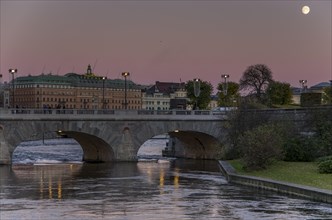 Evening view of a city with a bridge over a river and the moon in the twilight sky Stockholm