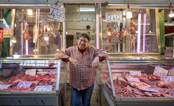 Butcher, meat trader posing proudly in front of his market stall, display of fresh meat, butchery,