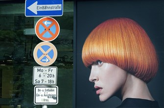 An advertising poster in the window of a hairdressing salon shows a photo of a woman with red hair.
