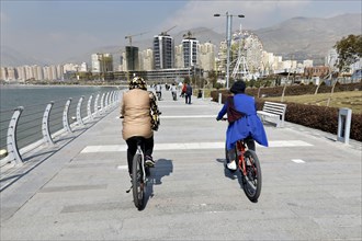 Two woman ride their mountain bikes at Lake Chitgar in Tehran, Iran. Lake Chitgar is an artificial