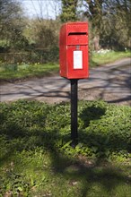 Red rural post box on its own at small road junction, Boulge, Suffolk, England, United Kingdom,