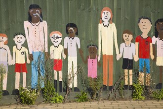 Mural painted on wooden fence of children of different ages holding hands, UK