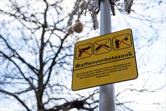 Yellow sign on a post with the inscription 'Weapons Prohibition Zone' and two crossed firearms,