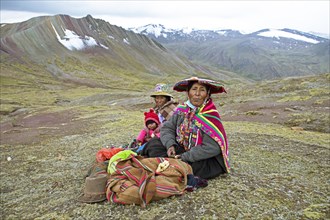 Peruvian woman, 55 and 27 years old, in traditional dress sit with a toddler, 7 months, in a field