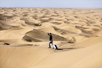 Symbolic image, tourist with suitcase in the desert, Mesr Desert, Iran. The Mesr Desert is part of