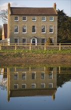 High House Farm farmhouse reflected in water of newly dug pond, Bawdsey, Suffolk, England, United
