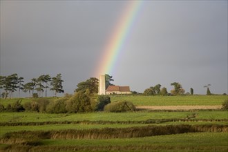 The end of a rainbow lights up the tower of All Saints church, Ramsholt, Suffolk, England, United