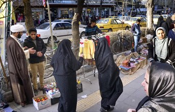 A mullah talks to a street vendor in Arak, Iran, woman wearing chadors and traditional dress on 16