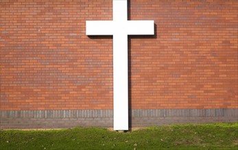 Large white crucifix cross against brick wall on grass lawn River of Life Church, Felixstowe,