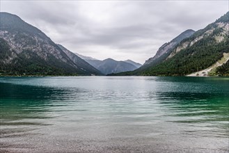 A peaceful lake surrounded by mountains under a cloudy sky, Plansee, Heiterwang, Tyrol, Austria,