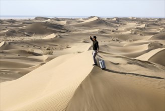 Symbolic image, tourist with suitcase in the desert, Mesr Desert, Iran. The Mesr Desert is part of