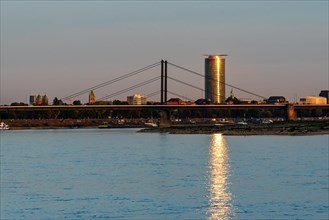 A river with a bridge and an illuminated skyscraper in the background at sunset,