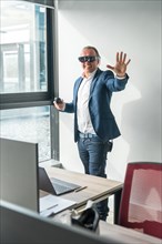 Vertical photo of a casual businessman gesturing using new mixed reality goggles in the office