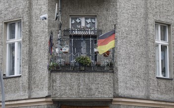 A German flag with a federal eagle flutters on the balcony of a run-down apartment building,