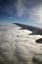 Aeroplane wing of plane cruising in blue sky high above clouds over Europe