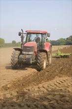 Tractor harrowing soil in field in preparation for planting, Shottisham, Suffolk, England, United