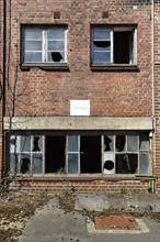 Empty dilapidated factory building, broken window panes, sign saying assembly, industrial ruin,