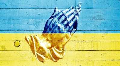 Ukrainian flag painted on a concrete wall with praying hands