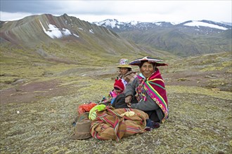 Peruvian woman, 55 and 27 years old, in traditional dress sit with an infant, 7 months old, in a