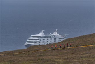 Passengers of the cruise ship Stella Australis in life jackets hike in storm and rain to Cape Horn,