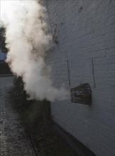 Heat steam emissions from domestic oil powered boiler heating system released through wall of house
