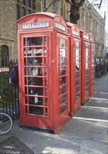 Four old red telephone boxes in the street, Cambridge, England woman walking into frame using a