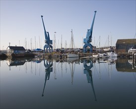 Two large blue industrial cranes reflected in water of Wet Dock marina, Ipswich, Suffolk, England,