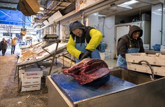 Fishmonger cutting up tuna in front of his market stall, display of fresh fish and seafood on ice,