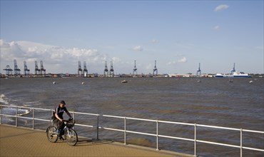 Man cycling on the seafront at Harwich, Essex, England with the Port of Felixstowe in the