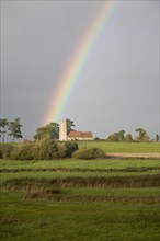 The end of a rainbow lights up the tower of All Saints church, Ramsholt, Suffolk, England, United